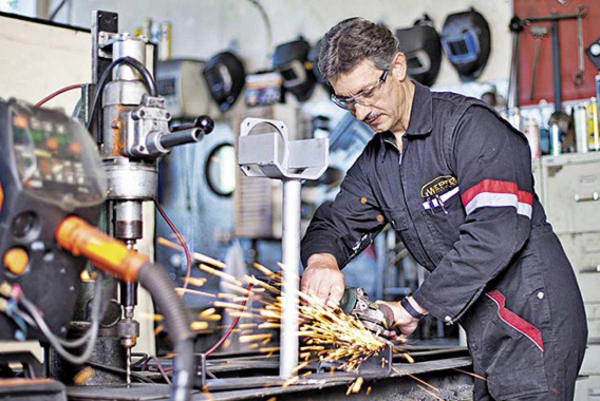Hans Wepfer dans son atelier. Au premier plan, des machines, à l'arrière-plan, Hans et un Flex au travail.
